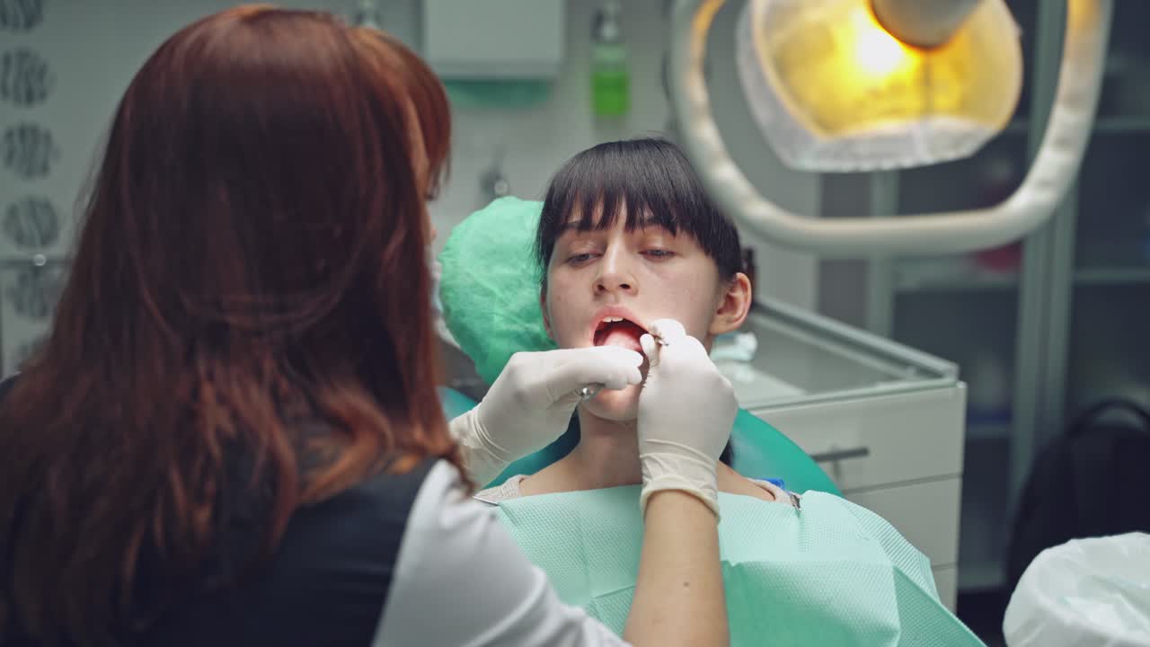 A dentist examines the oral cavity of a young client, who is sitting on the dental chair in the office. Close-up.