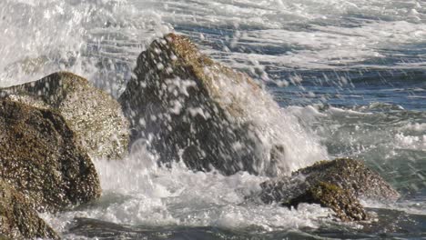 Wave-breaking-over-rocks-into-white-spray,-close-up