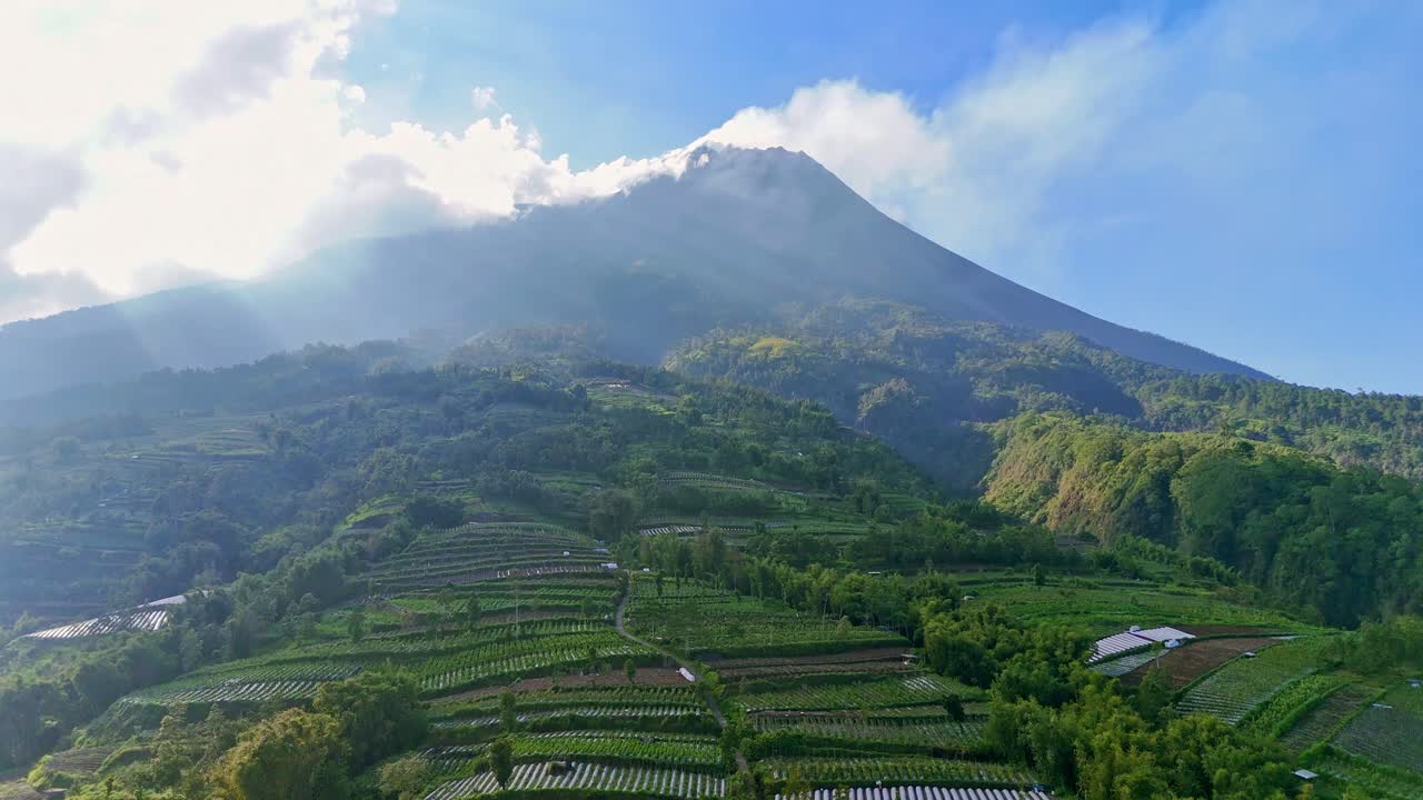Aerial view of sunny morning on the tropical indonesia countryside, slope of Merapi Volcano. Sun lighting up beautiful tropical countryside with mountain background. 4K drone footage.
