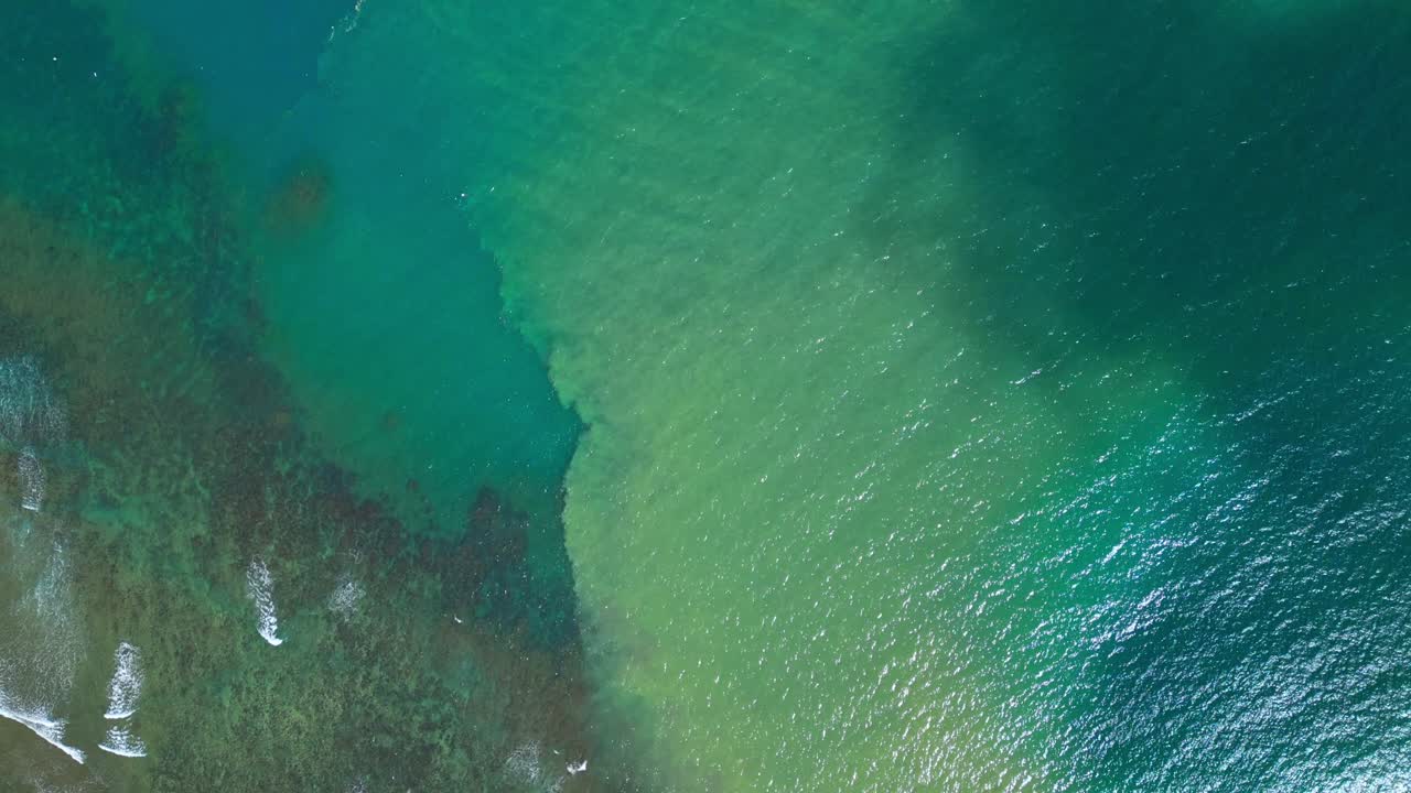 An overhead aerial of the sea in Aurora, Philippines, highlighting a striking color division where blue green shallows meet deeper turquoise waters, with waves rolling across the vivid contrast
