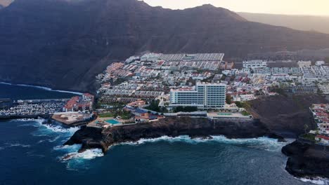 Dron-shot-of-coast-line-with-houses-and-huge-mountain-in-the-background,-Spain