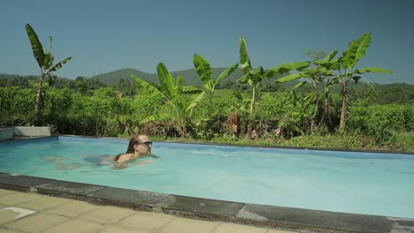 tipo caucásico nadar en la piscina rodeado de árboles tropicales, slowmo