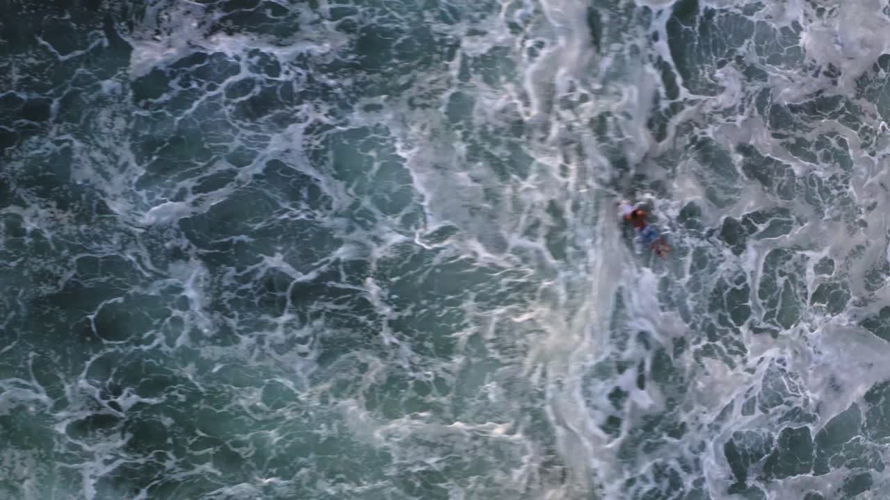 Aerial: surfer paddling in breaking wave whitewater, bird's eye view