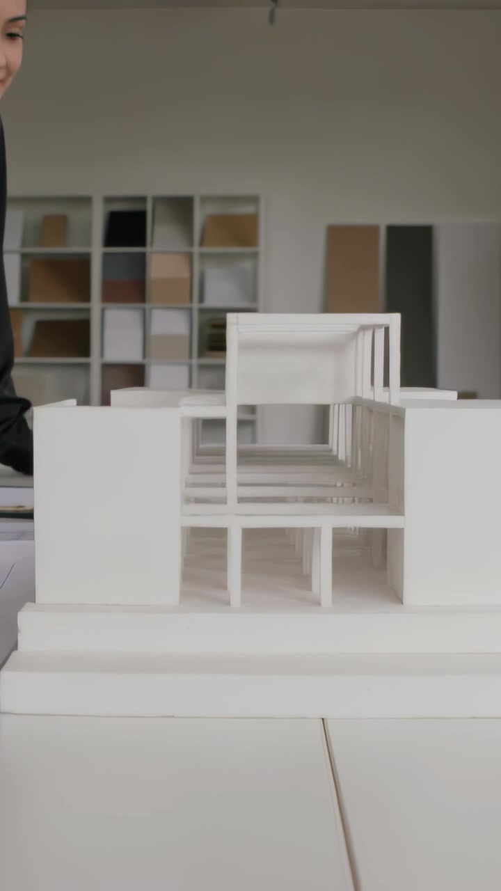 Video verticale: Regolando un modello bianco, una designer con maglia nera indica un corridoio per la revisione in studio.
