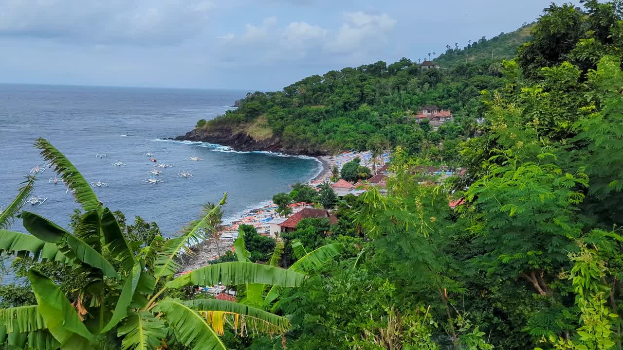 Scenic aerial view of sheltered bay, ocean, and local fishing boats on beach surrounded by green trees at Easternmost Point of Bali, Indonesia
