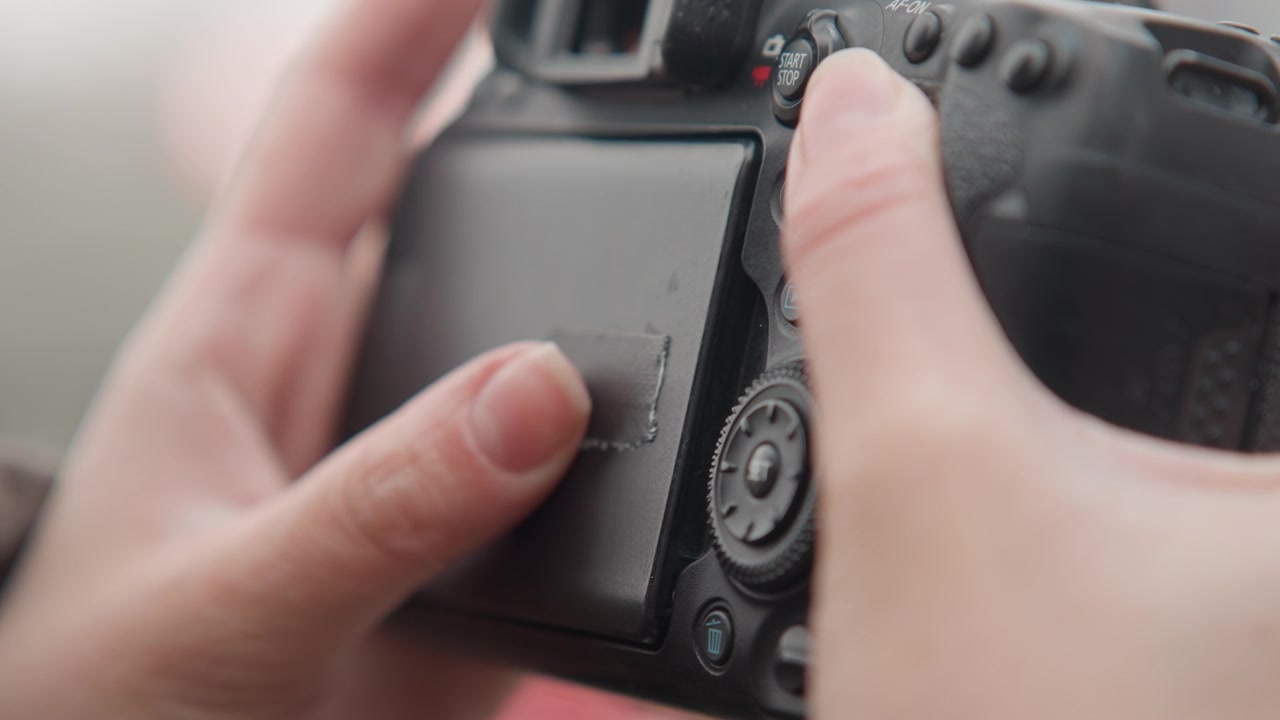 Nahaufnahme von Händen, die einen Kamera-LCD-Bildschirm bedienen; Fotograf überprüft Einstellungen, navigiert im Menü, passt Belichtung und Fokus an, drückt Tasten und dreht Einstellräder, überprüft die Wiedergabe auf dem schwenkbaren Display in Ruhe