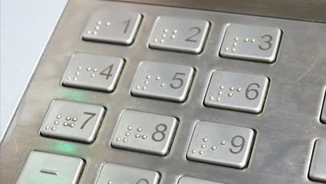 close-up of a steel atm keyboard panel and a hand typing pin code on it