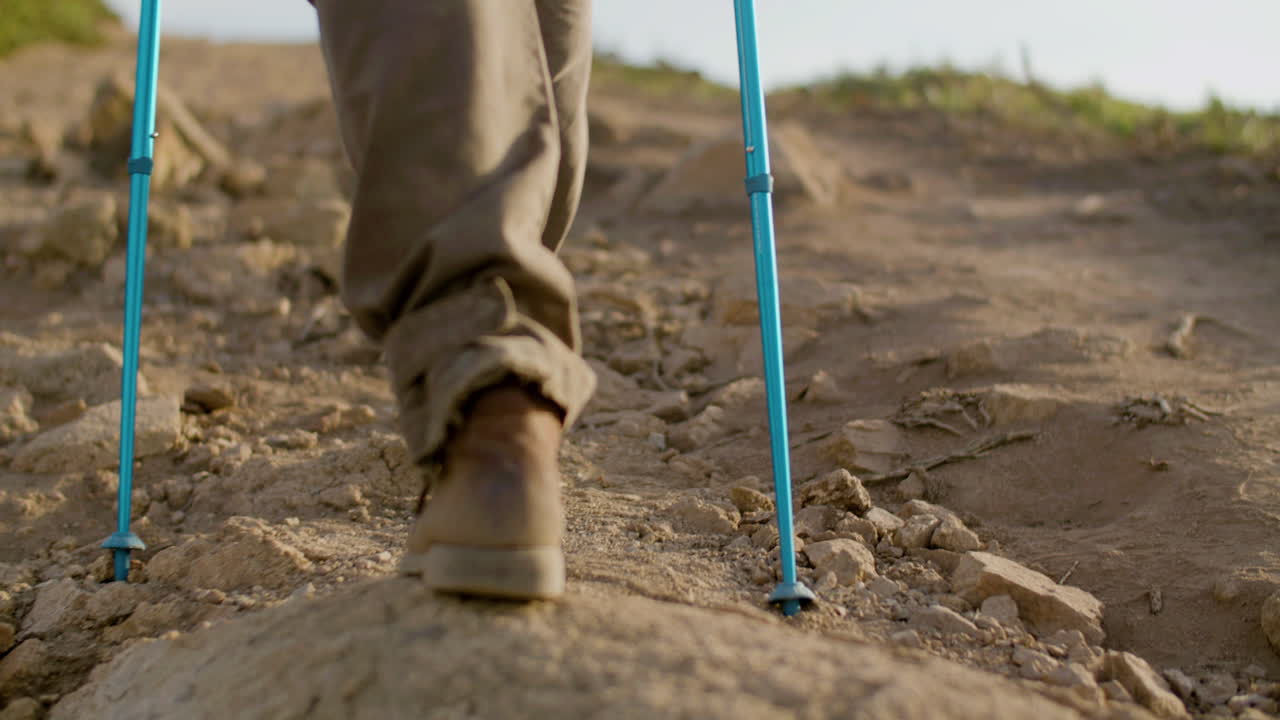 vista trasera de un excursionista irreconocible escalando una montaña con bastones de trekking