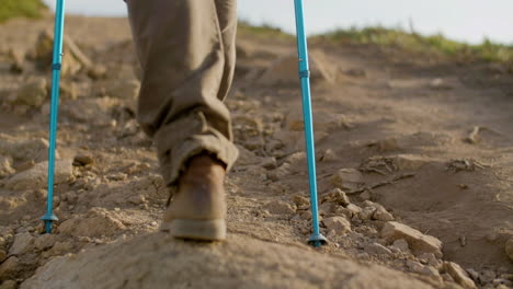 back view of an unrecognizable hiker climbing mountain with trekking poles