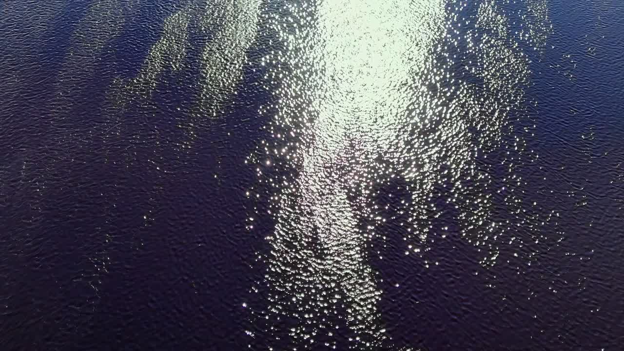 클로즈업 드론은 자연 요소 위의 파란 물 빛에 반사되는 빛을 날아갑니다.