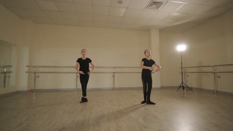 a group of young ballet students in black dancewear practicing positions in a spacious ballet studio with wooden flooring and wall-mounted barres. focused expressions and synchronized movements.