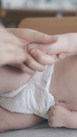 cute fair haired newborn boy in white diaper lies on side on changing table and nurse practices arm massage close view