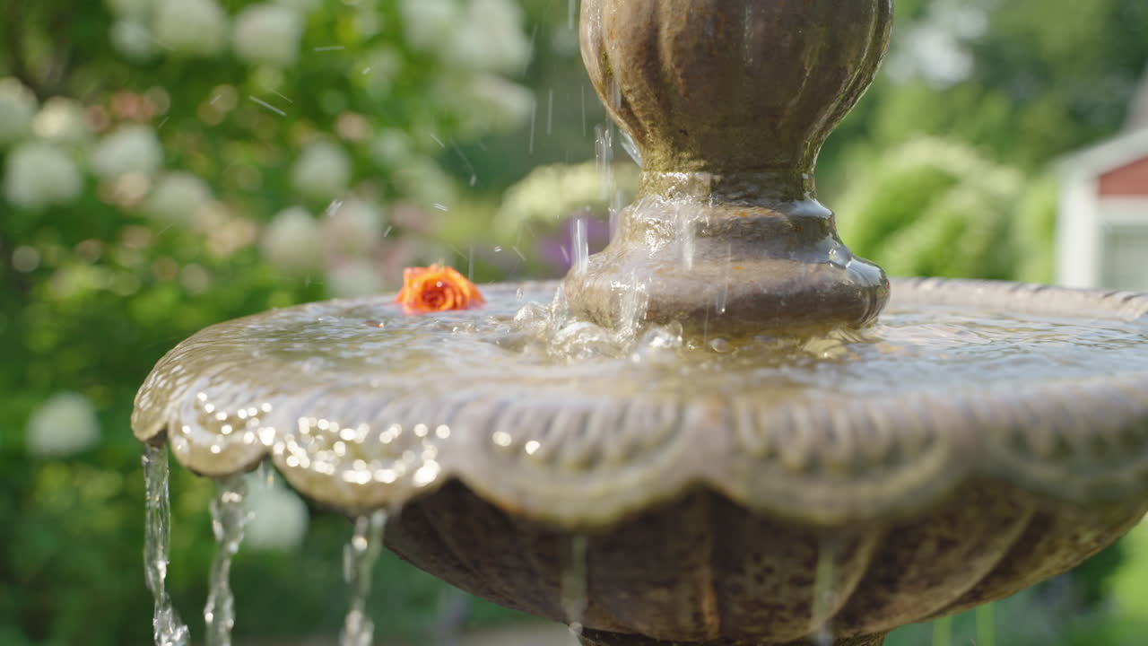 꽃이 피는 꽃으로 둘러싸인 물이 떨어지는 정원 분수의 클로즈업
