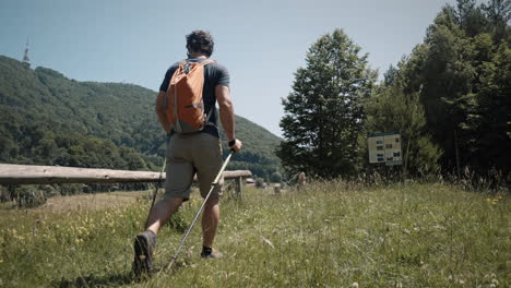 man with backpack walking with poles towards mountain bo?