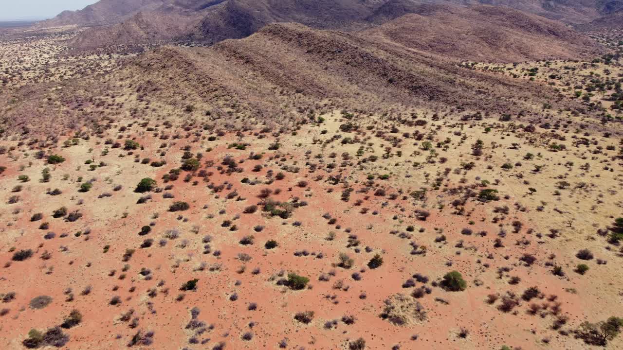 Vista aérea da savana africana com árvores e gramíneas espalhadas em areia vermelha árida do Kalahari e montanhas rochosas, Cabo Setentrional, África do Sul.