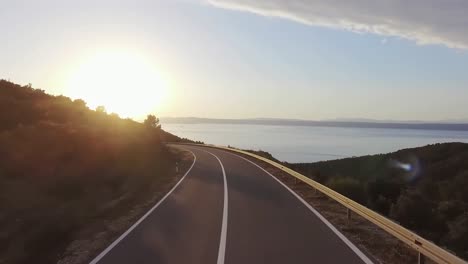 drone flying over a road in portugal and slowly rising higher and going off the road while the sun is setting in the evening time