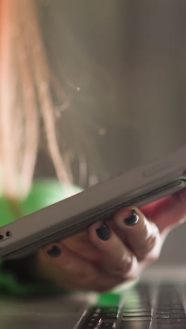 una mujer con un suéter verde sosteniendo y haciendo clic en su teléfono inteligente mientras una computadora portátil está delante de ella. capturado con una cámara de mano, haciendo hincapié en la multitarea y el espacio de trabajo digital moderno