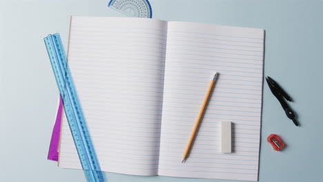 vista aérea de un cuaderno abierto con papelería escolar en fondo azul, en cámara lenta