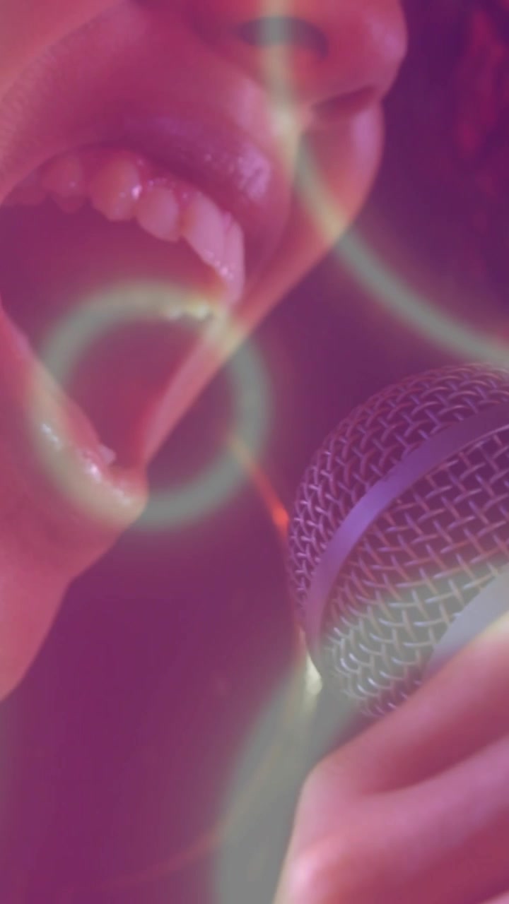 Video verticale: Cantante donna che si china verso il microfono, creando anelli al neon e potenziando la voce per la musica.