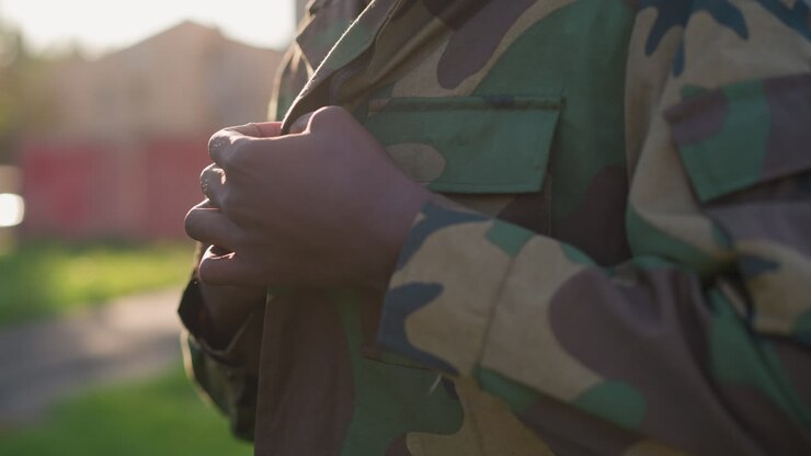 Preparazione militare notturna, soldato che modifica la giacca mimetica, sfondo urbano sfocato mentre il soldato si prepara per l'operazione, uomo in mimetica durante il tramonto che modifica l'uniforme prima di intraprendere una missione segreta