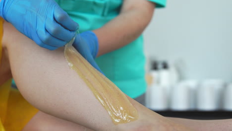 Two-girls-in-a-beauty-salon-master-in-a-Bathrobe-and-gloves-doing-the-procedure-to-remove-hair-on-the-legs-with-a-sugar-mixture