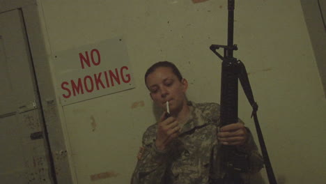 a solider lights a cigarette in front of a no smoking sign