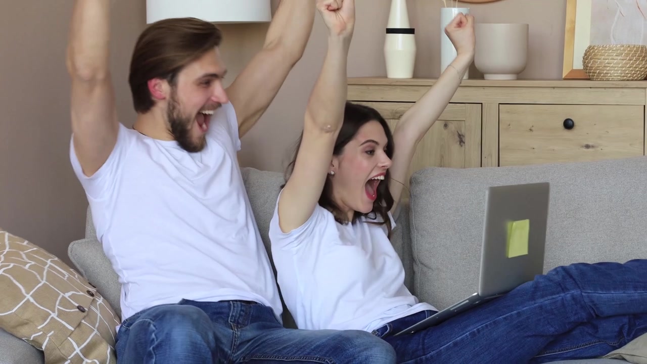 Giovane coppia entusiasta celebra il successo mentre usa il laptop a casa