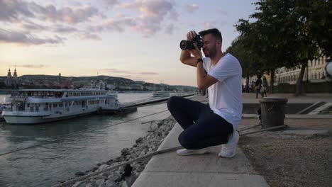 Imágenes-De-4k-De-Un-Joven-Tomando-Fotos-Mientras-Se-Pone-El-Sol-Con-Una-Cámara-Réflex-Digital-Profesional-Junto-Al-Río-Donau-En-Budapest,-Hungría