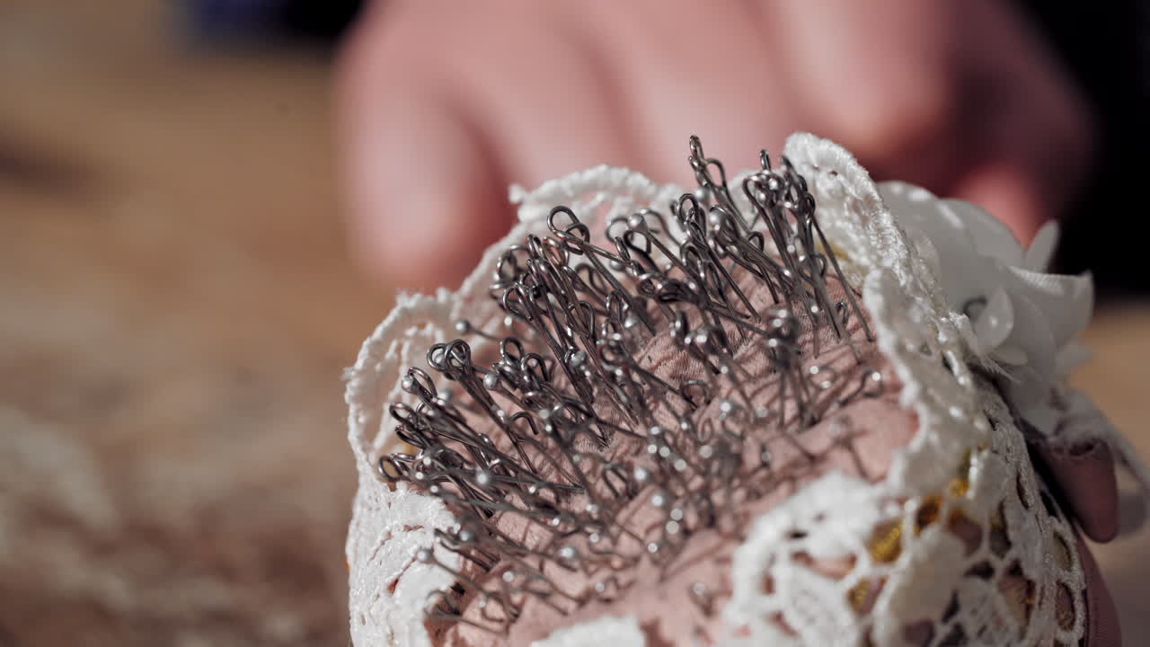 Hand of a seamstress is taking pin from workplace in atelier. Many black sewing pins in special pin pillow on a table. Close-up.
