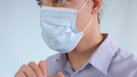 male with a man bun and smoldering eyes wearing a button down shirt puts on a covid-19 - coronavirus surgical mask on a grey background, side angle static shot