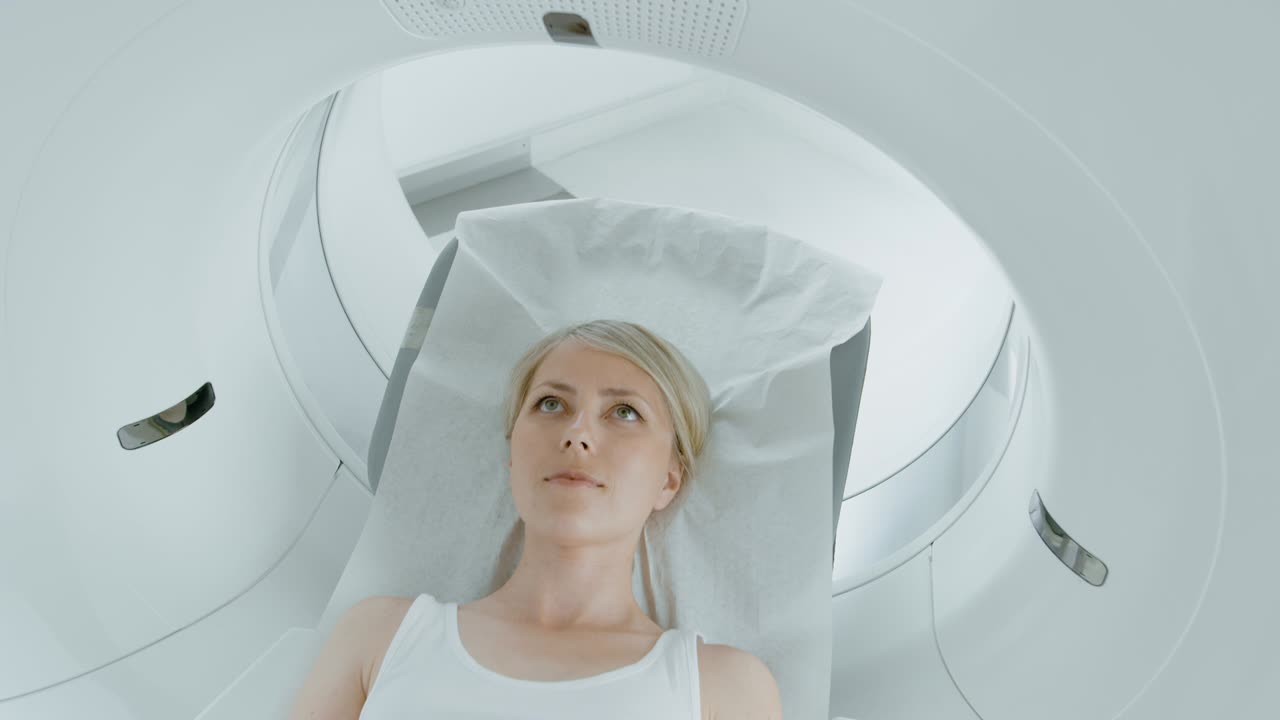 retrato en primer plano de una paciente que yace en una tomografía computarizada o resonancia magnética, la cama se mueve dentro de la máquina escaneando su cuerpo y cerebro. en un laboratorio médico con equipos de alta tecnología. toma de cámara elevada.