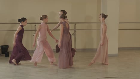 a group of young ballet students in black dancewear practicing positions in a spacious ballet studio with wooden flooring and wall-mounted barres. focused expressions and synchronized movements.