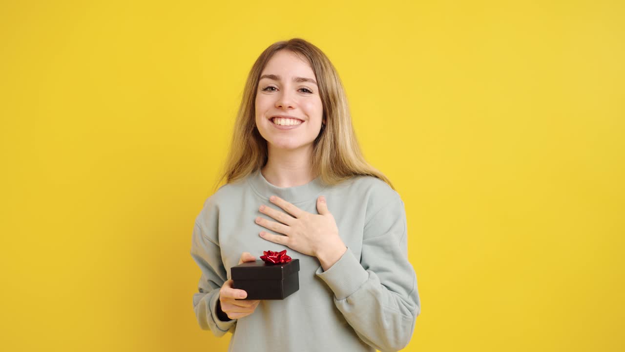 Young woman offering a gift on yellow background