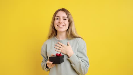 young woman offering a gift on yellow background
