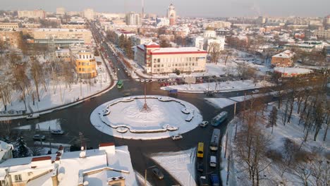 4k aerial view of roundabout road with circular cars in snow covered small european city at winter sunset