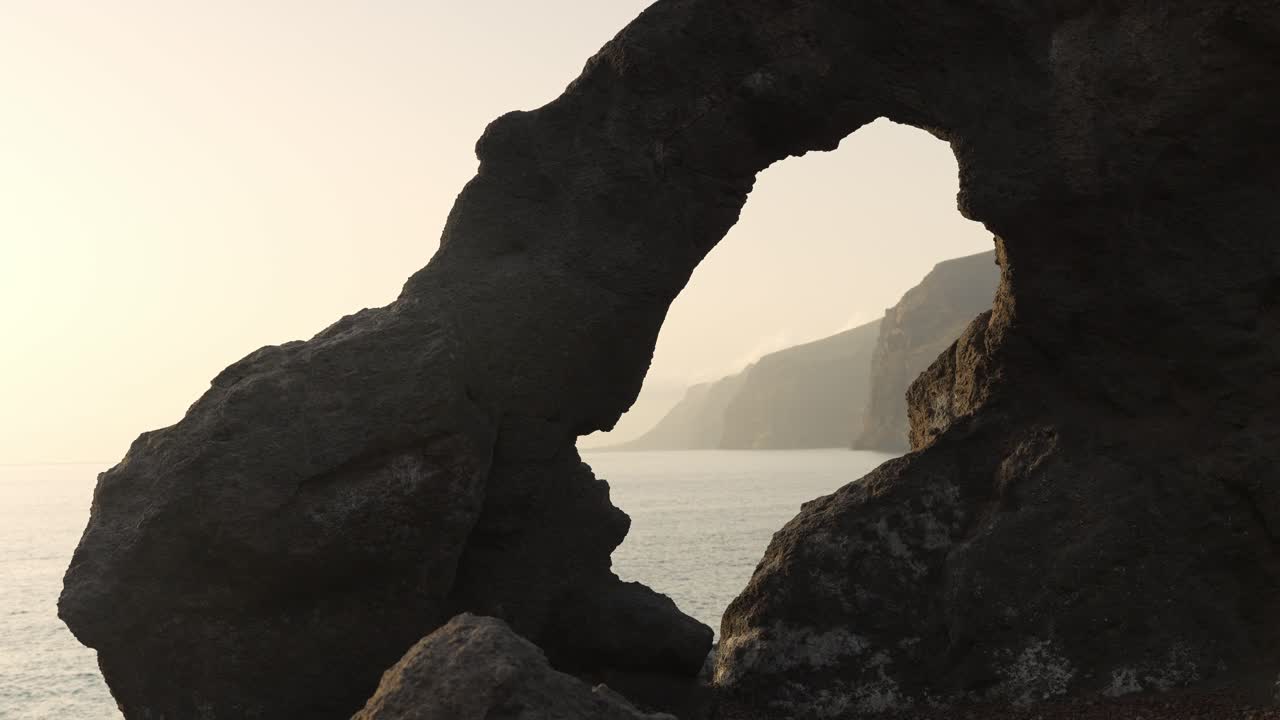 Golden-hour glow illuminates ocean behind framing rock formation