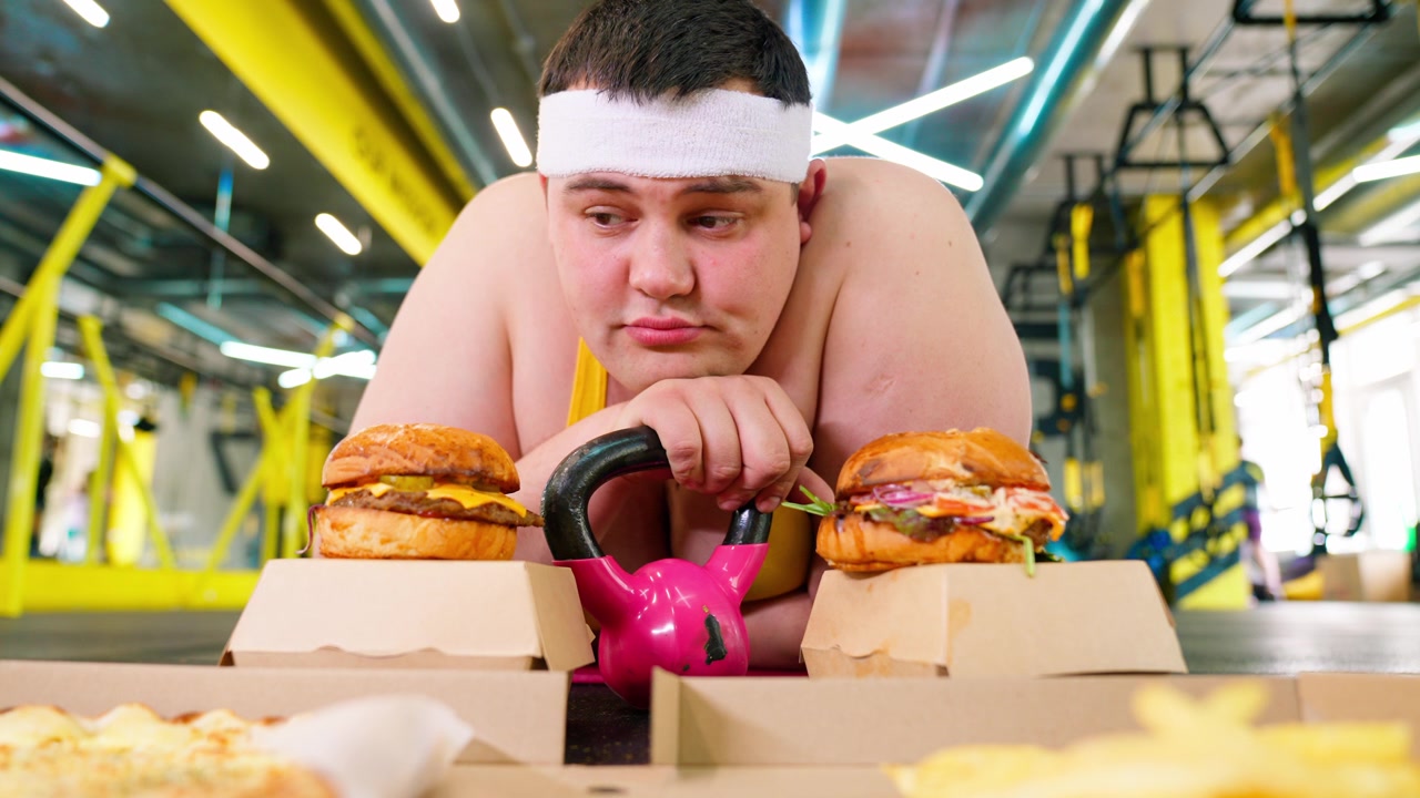 Uomo in sovrappeso che lotta con la tentazione del fast food in palestra