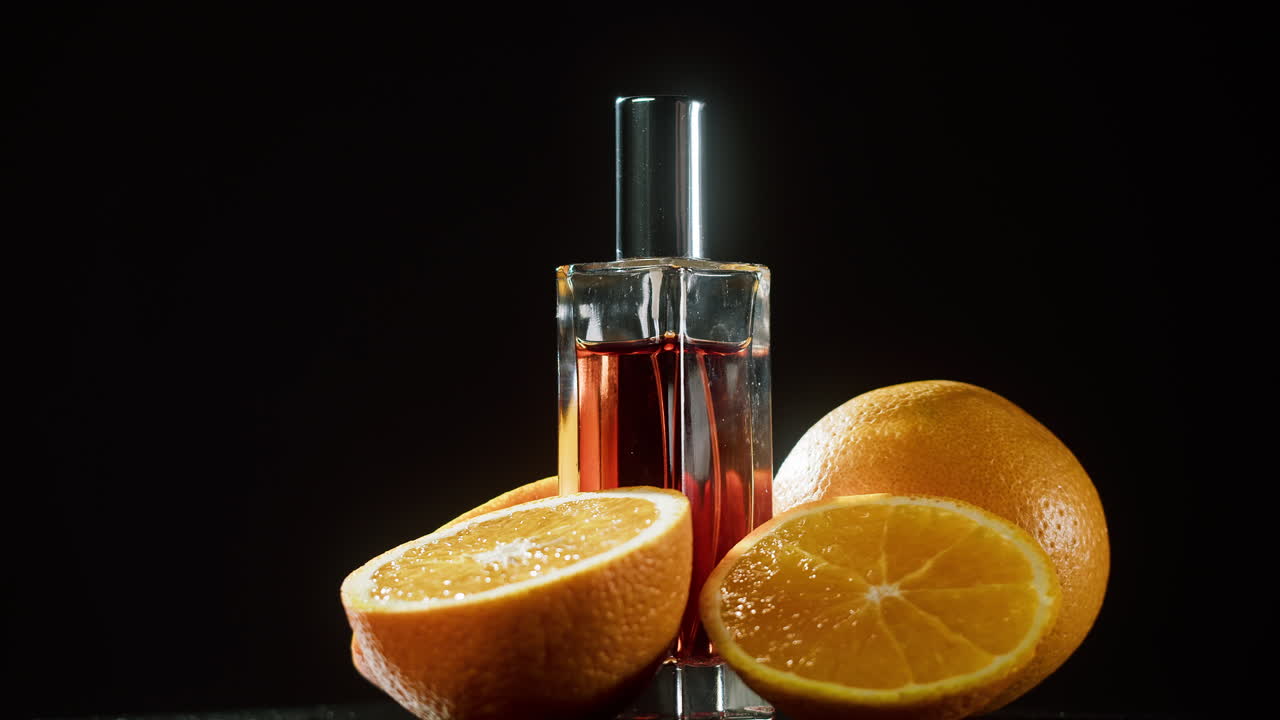 Flacone di profumo con arance fresche che ruotano su sfondo nero
