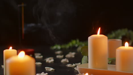 still life of lit candles with scattered flower petals and incense stick against dark background as part of relaxing spa day decor