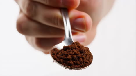 hand holding a spoon with coffee grounds falling