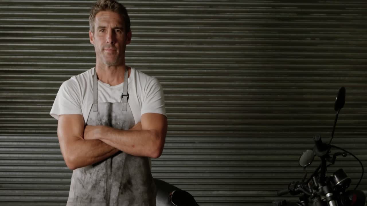 mecánico masculino de pie con los brazos cruzados en un garaje de reparación de motocicletas 4k
