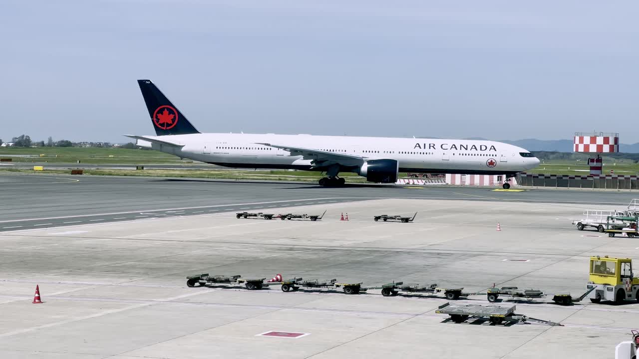 Air Canada Boeing 777 aircraft taxis on the runway, preparing for departure. The scene captures airport operations with towing equipment and a clear view of the surrounding airfield