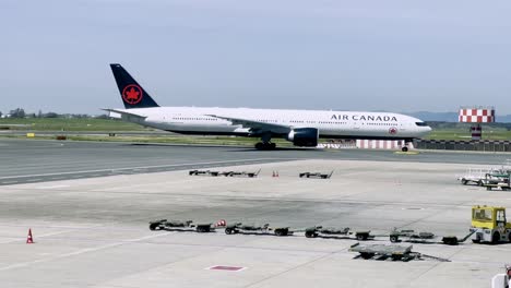 air canada boeing 777 aircraft taxis on the runway, preparing for departure. the scene captures airport operations with towing equipment and a clear view of the surrounding airfield