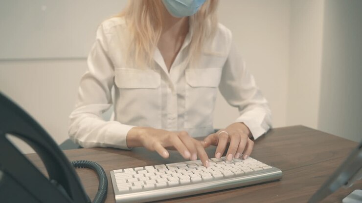 Primo piano di una professionista con mascherina che lavora al computer in ufficio.
