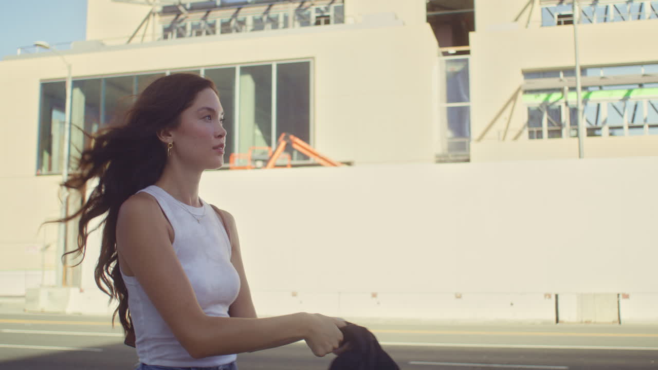 una mujer tranquila caminando con una chaqueta en un hombro. una chica asiática bajando por la calle.