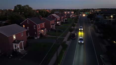 houses and apartments along street with traffic at dusk. small american town in the evening. red brick american neighborhood with porch. aerial birds eye. wide shot.