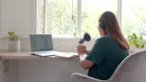 Mujer-Birracial-De-Talla-Grande-Usando-Audífonos,-Laptop-Y-Micrófono-Podcasting,-Espacio-Para-Copiar,-Cámara-Lenta