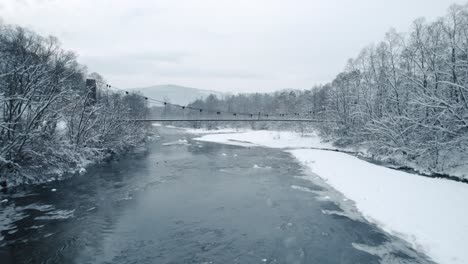 aerial shot of frozen river with swimming ducks, hanging bridge and walking man in the winter season