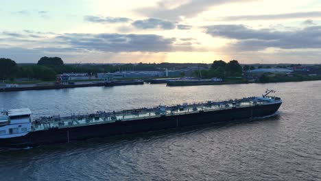 oil tanker ship sailing along river waterway, aerial tracking side view