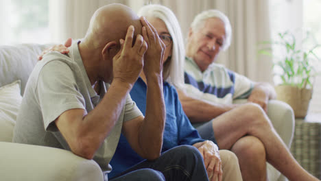 una pareja caucásica anciana consolando a un amigo varón anciano triste y diverso en la sala de estar, en cámara lenta.